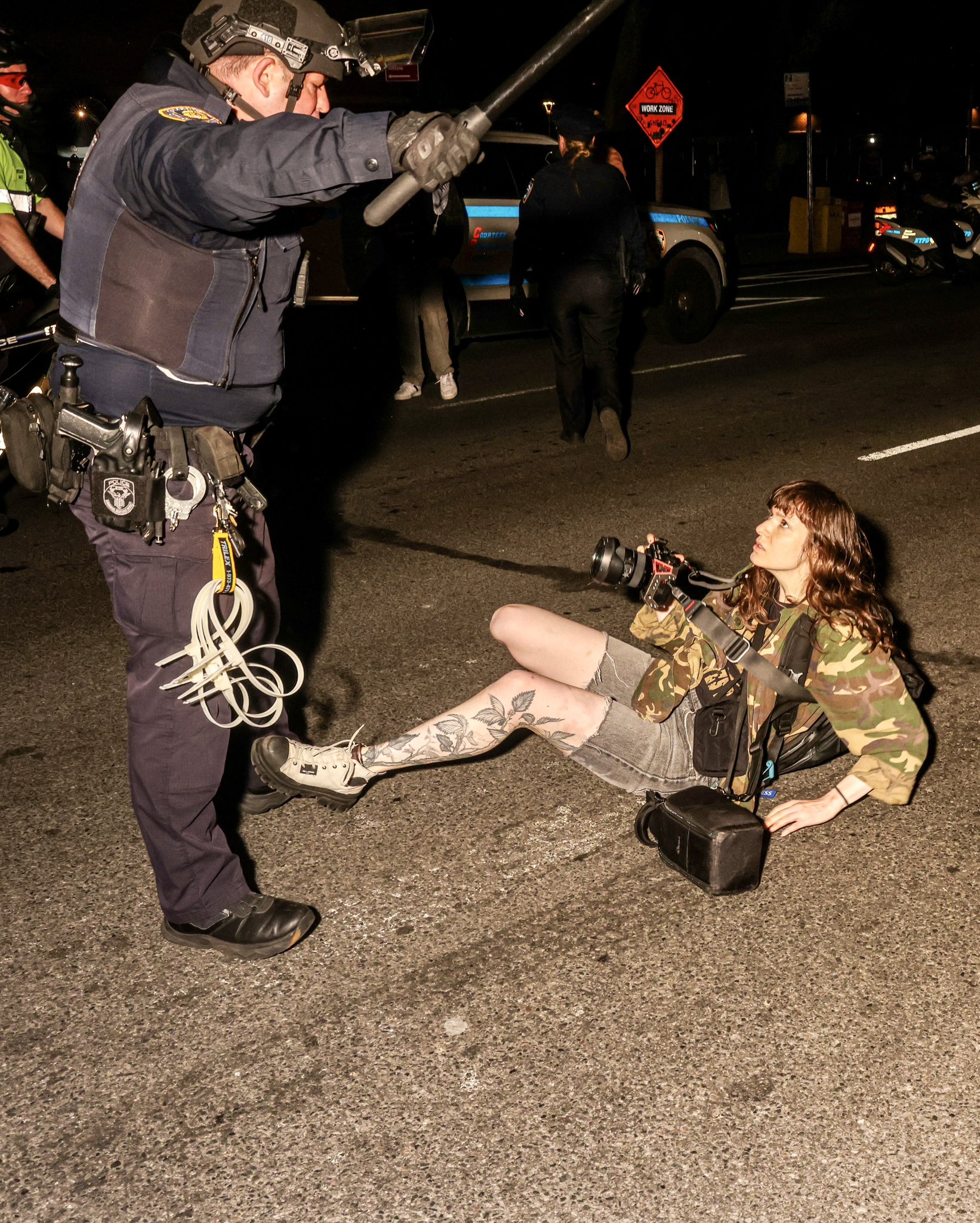 A police officer in riot gear swinging his baton over journalist Olga Fedorova after having pushed her to the ground, shortly before her arrest. Fedorova is staring defiantly back at the cop, still pointing her camera at him. Photo credit Alex Kent (alex-kent.com, via twitter @AlexKentTN)