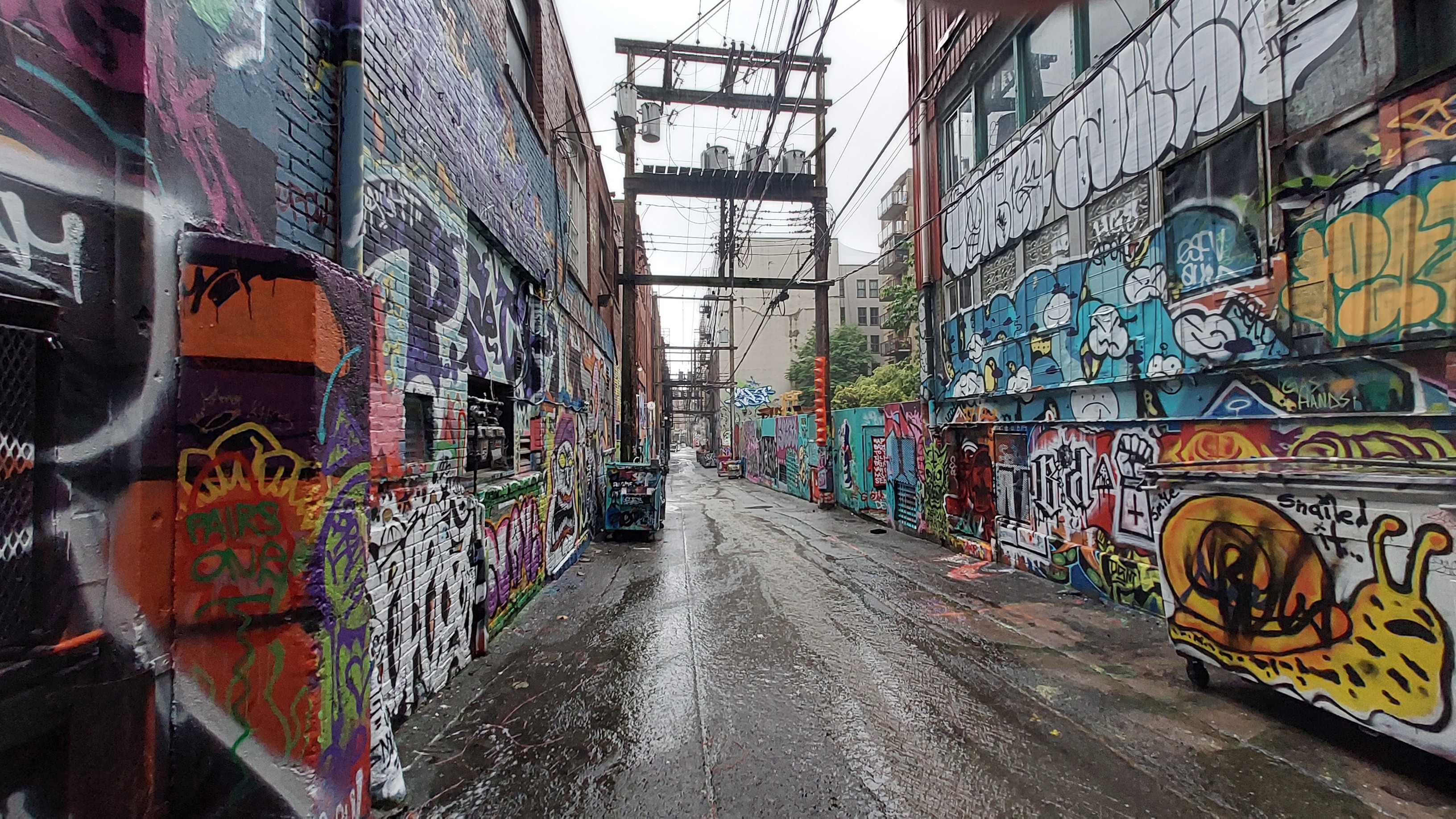 Wide angle photo of an urban back alleyway, with ample amounts of colourful graffiti on either side.