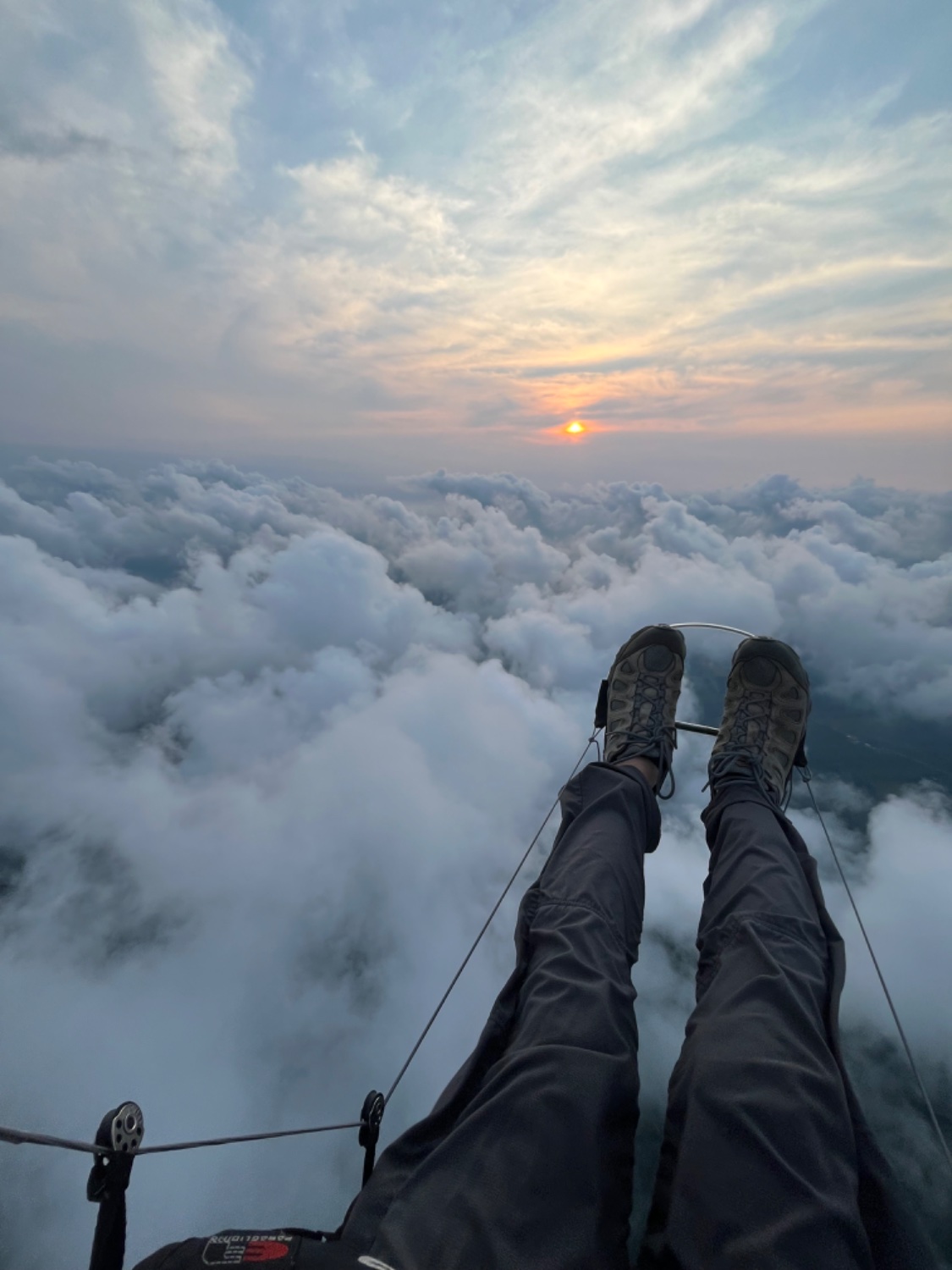 Flying above clouds in paramotor. Legs with boots pushing on a paramotor speed bar. Sun is low in sky and obscured by layers of clouds.